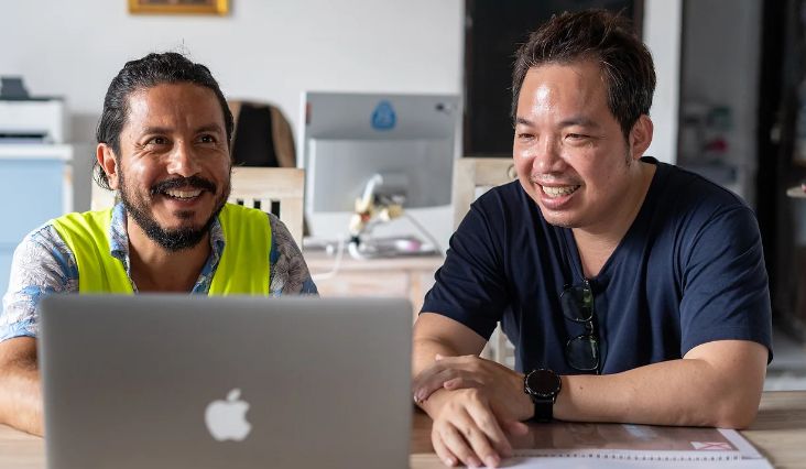 Photograph of two workers smiling sitting at a laptop computer